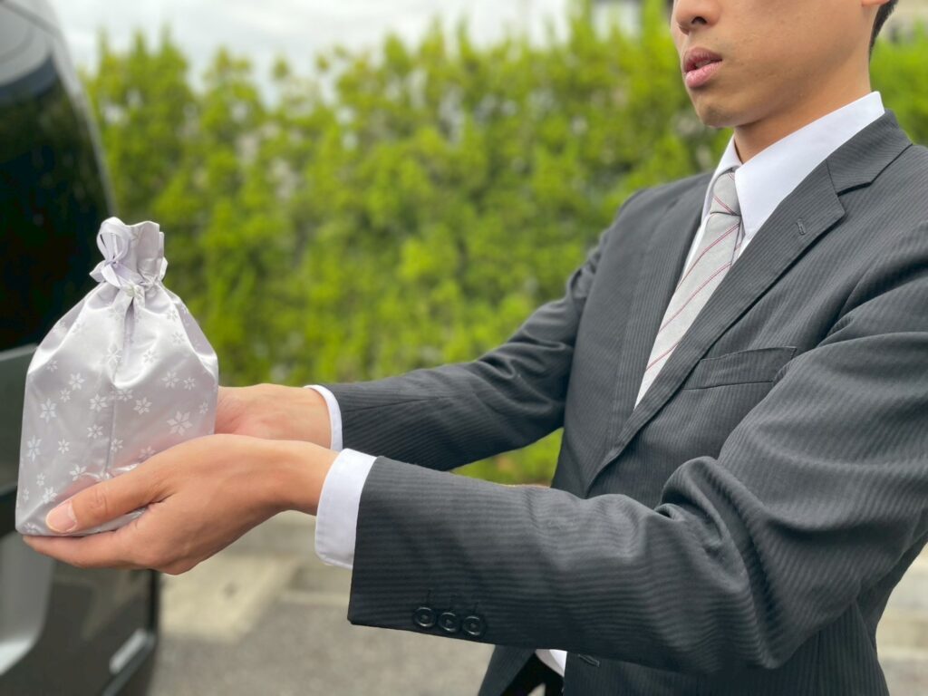 グレーのビジネススーツを着た男性がピンク色の花柄ギフトバッグを両手で持っている屋外の写真