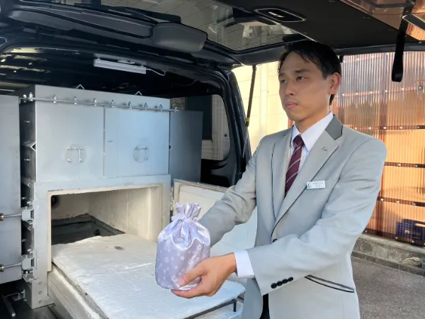 白いビジネススーツを着た男性が車の冷蔵ボックスから紫色の保冷バッグを取り出している