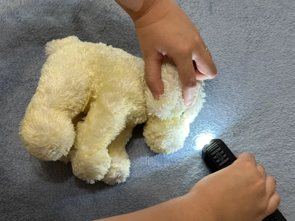 黄色いぬいぐるみ子犬に光を当てて遊ぶ子どもの手