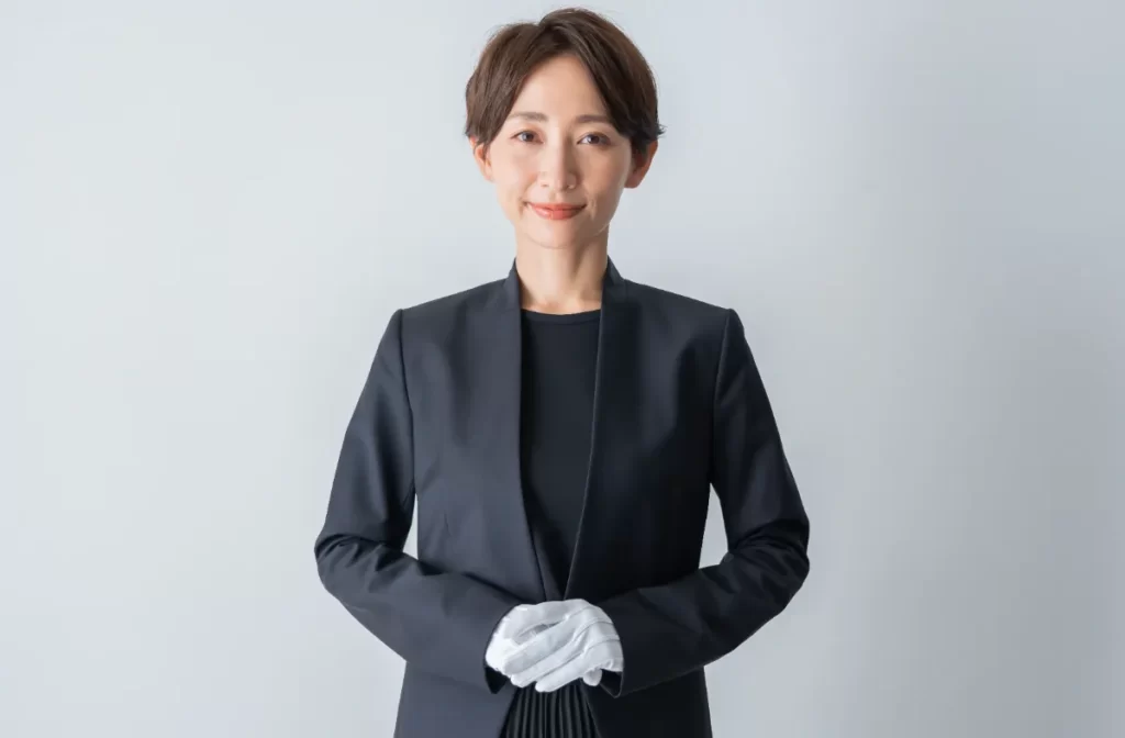 黒いスーツと白手袋を着用した女性が正面を向いて立っている