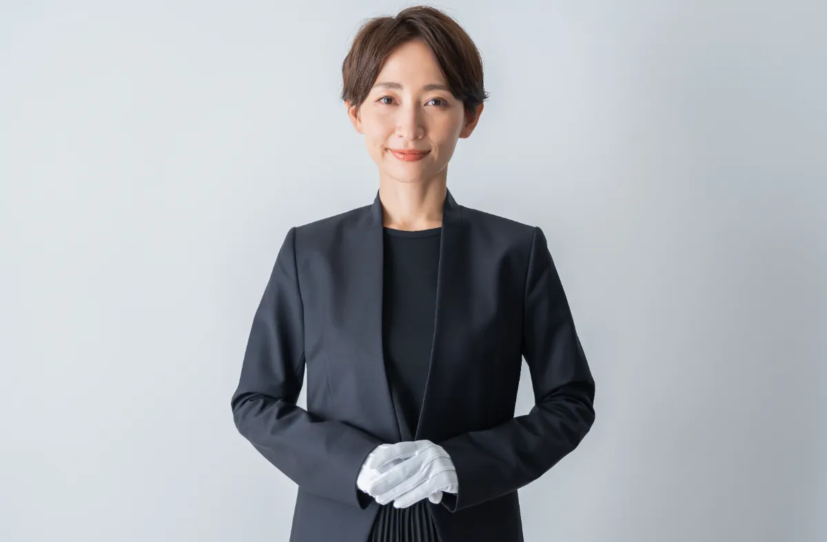 黒いスーツと白手袋を着用した女性が正面を向いて立っている